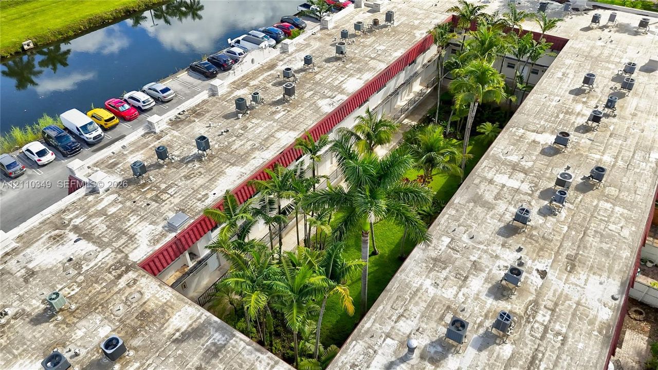 Aerial view featuring a multi-unit property with a central landscaped courtyard, mature palm trees, designated surface parking, and waterfront proximity