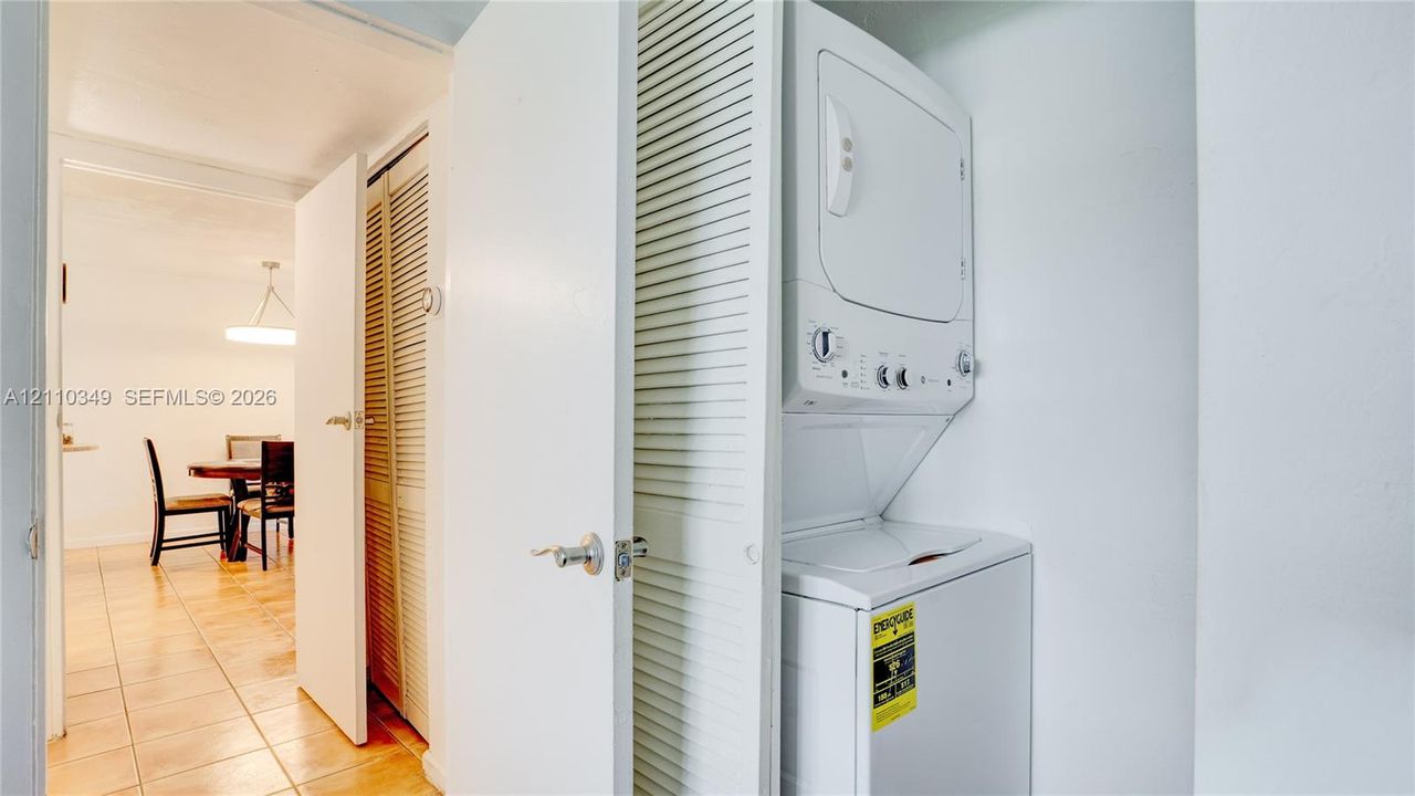 Stackable laundry unit housed within a closet featuring white louvered doors