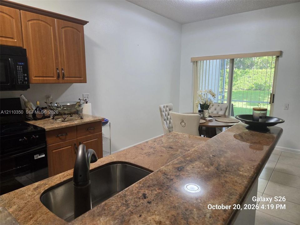 Kitchen featuring stained wood cabinetry, stone-finish countertops, stainless steel undermount sink with a high-arch faucet, black built-in microwave, and tile flooring