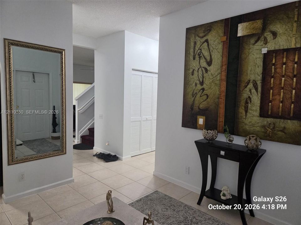 Foyer featuring neutral tile flooring, white wall-mounted louvered closet doors, and a wall-mounted decorative mirror
