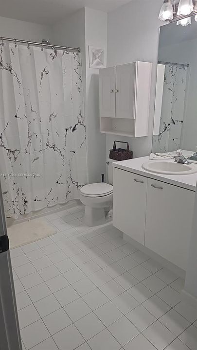 Bathroom featuring white tile flooring, white vanity cabinet with integrated sink, wall-mounted storage cabinetry, and a full-width mirror