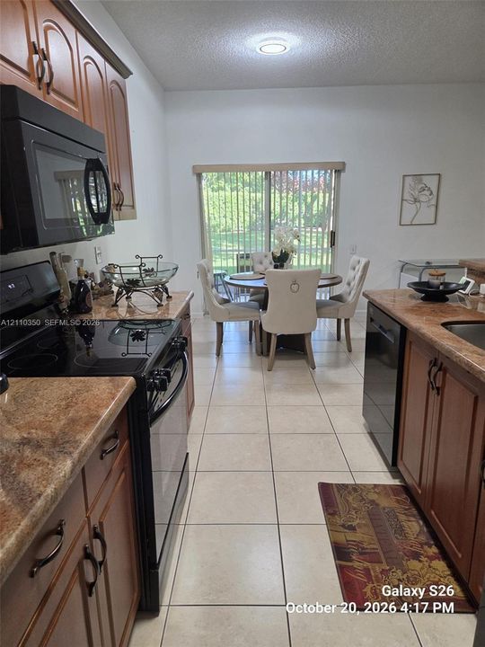 Kitchen featuring wood-finish cabinetry, stone-finish countertops, black built-in appliances, ceramic tile flooring, and a sliding glass door