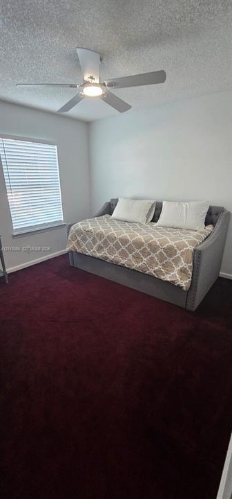 Room featuring plush carpeting, a multi-blade ceiling fan with integrated lighting, and a single-hung window with horizontal blinds