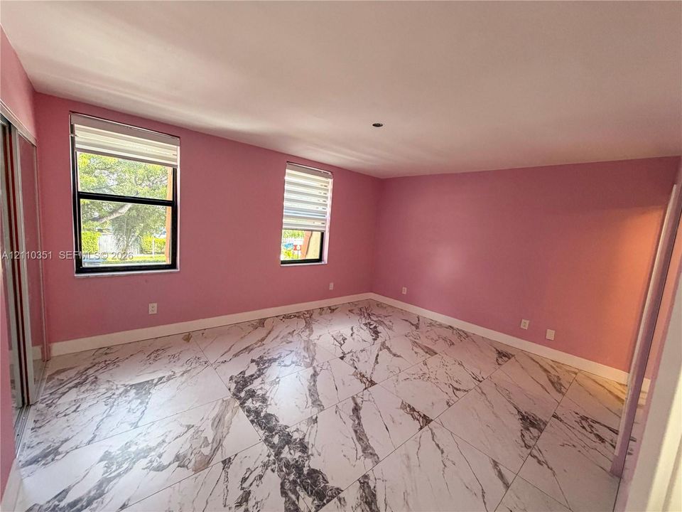 Interior room featuring large-format tile flooring with a veined pattern, two windows with horizontal blinds, and mirrored sliding closet doors