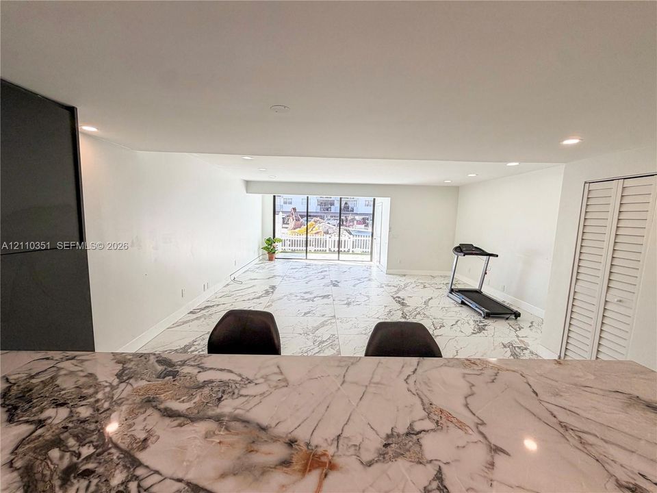 Open-concept interior featuring large-format stone-finish flooring, recessed ceiling lighting, louvered closet doors, and floor-to-ceiling sliding glass doors