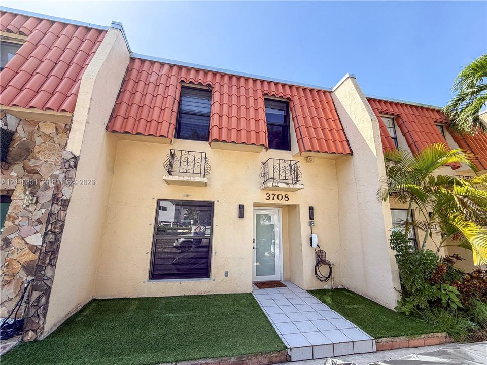 Exterior facade featuring stucco siding, red clay tile roofing, decorative wrought-iron balcony railings, and stone masonry accents