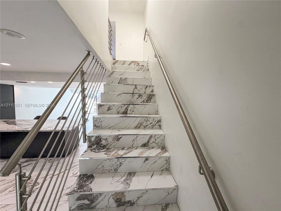 Staircase featuring stone-finish treads and risers, complemented by stainless steel railings with horizontal cable balusters and matching wall-mounted handrails