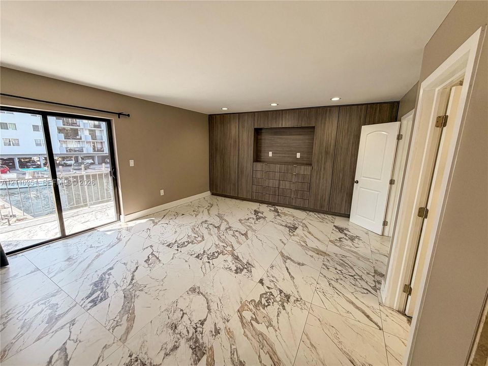Large-format porcelain tile flooring with veining, floor-to-ceiling wood-finish built-in cabinetry, recessed lighting, and sliding glass doors