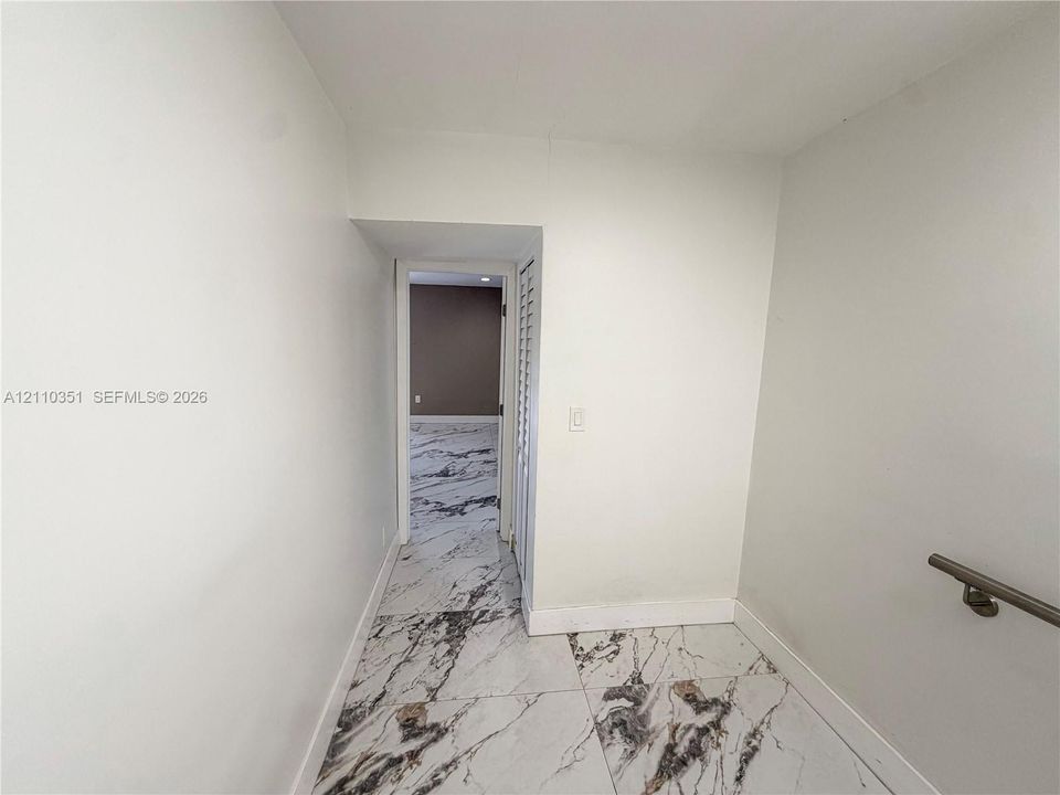 Large-format stone-finish flooring with veining, louvered closet door, and wall-mounted metallic handrail