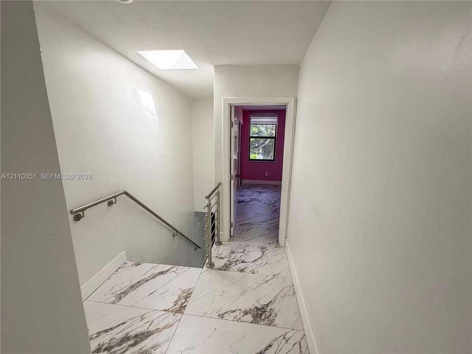 Large-format stone-style tile flooring with neutral veining, metal-finish handrails, and a skylight