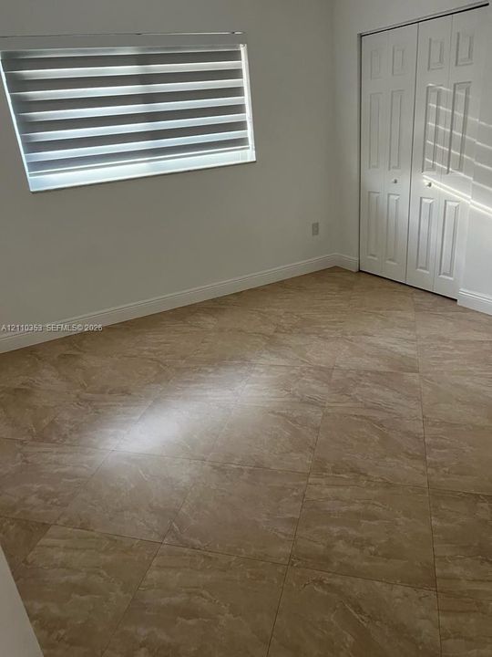 Large-format tile flooring set on the diagonal, featuring a dual-panel closet with six-panel doors and a multi-tiered horizontal window treatment