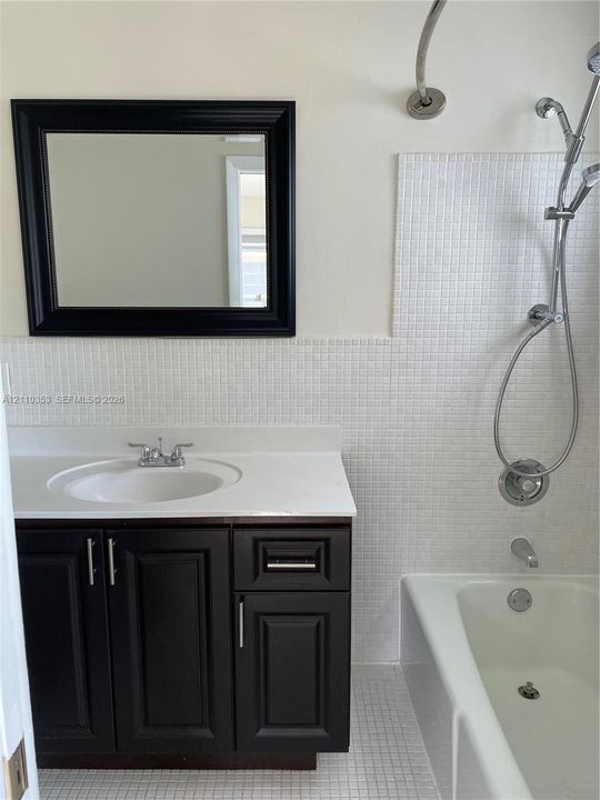 Bathroom featuring a dark wood-finish vanity with a white countertop, undermount sink, mosaic tile surround, and an adjustable handheld shower fixture