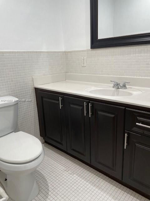 Dark wood-finish cabinetry featuring brushed nickel hardware, solid-surface countertop with an integrated basin, chrome dual-handle faucet, and mosaic tile wall accents