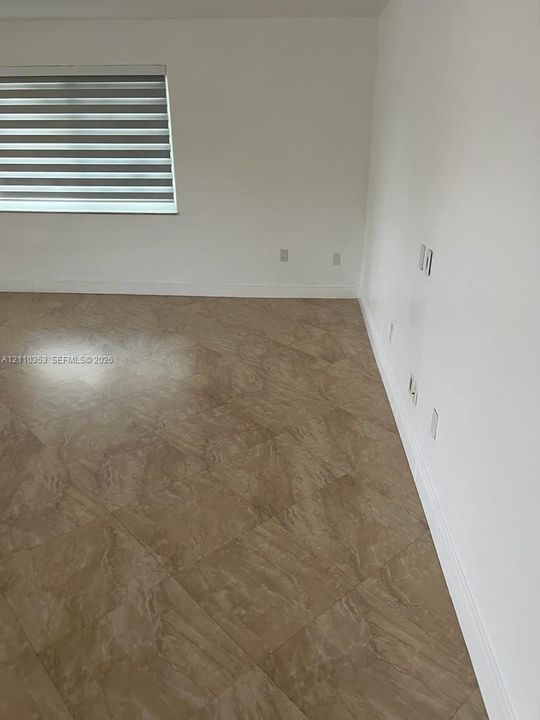 Neutral-toned interior space featuring polished tile flooring laid on a diagonal, crisp white walls, and a window fitted with horizontal dual-layer shades