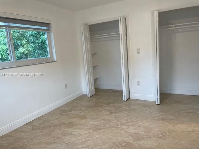 Neutral tile flooring, dual closets with bi-fold doors, built-in shelving, and a horizontal window with adjustable roller shade