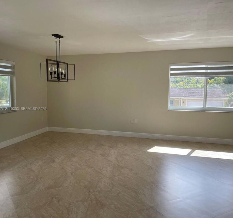 Neutral-toned interior space featuring light-colored stone-finish flooring, dual windows with contemporary horizontal blinds, and a geometric metal chandelier