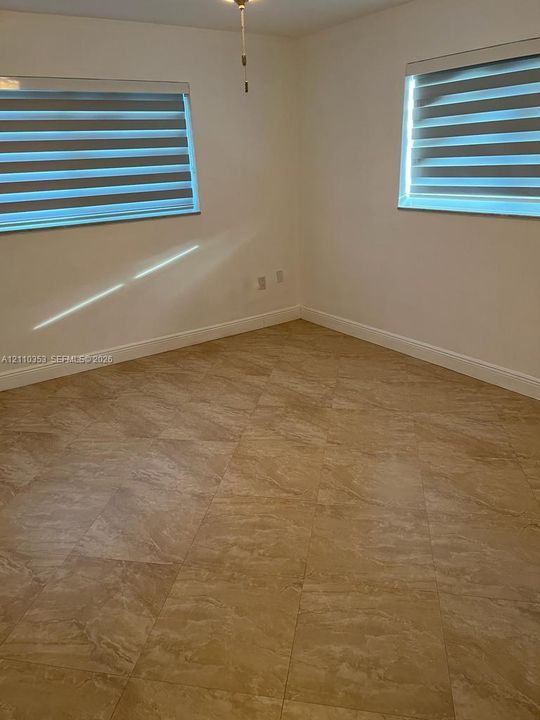 Neutral-toned tile flooring, dual windows featuring horizontal privacy blinds, and central overhead lighting