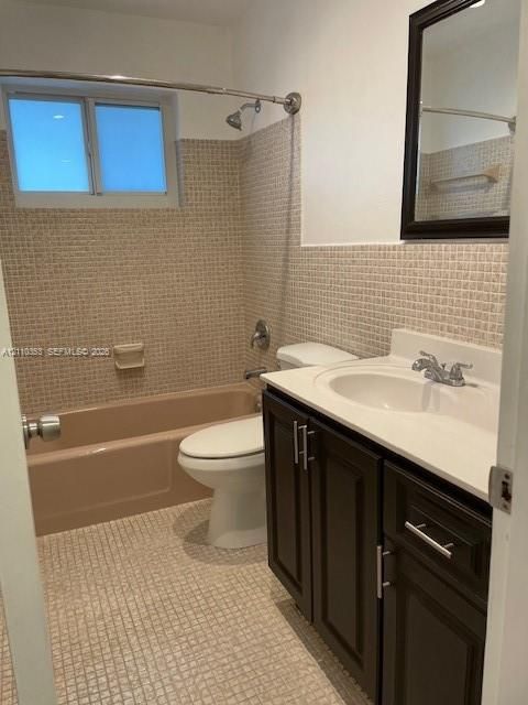 Bathroom featuring a dark wood-finish vanity with a white integrated countertop, textured square tile wall detailing, a classic bathtub, and a framed mirror