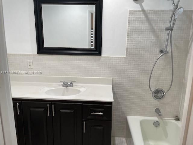 Bathroom featuring a dark-finish wood vanity, integrated solid-surface countertop, rectangular wall-mounted mirror, and tile-surround tub with a handheld shower fixture