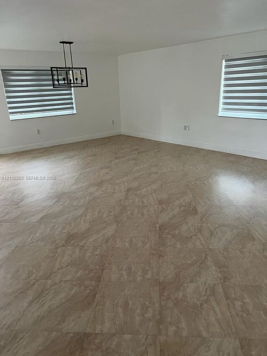 Neutral-toned large-format tile flooring, tiered window shades, and a geometric multi-light pendant fixture