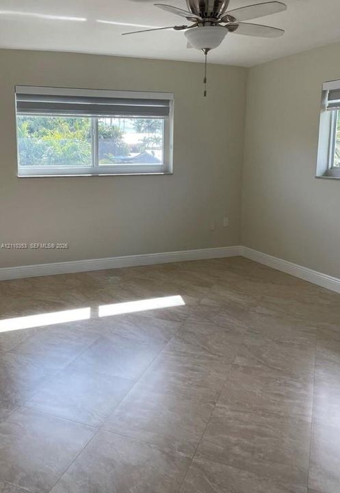 Neutral-toned interior space featuring stone-style tile flooring, dual windows with fitted shades, and an overhead ceiling fan