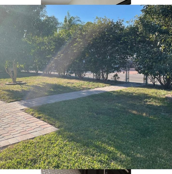 Backyard featuring a paved stone walkway, established trees, grass lawn, and a chain-link fence with a gate