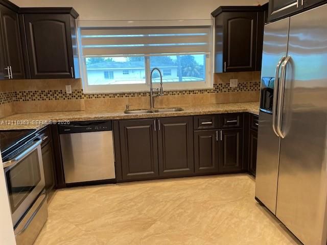 Kitchen featuring dark wood cabinetry, stainless steel appliances, stone-finish countertops, decorative tile backsplash, and large-format tile flooring