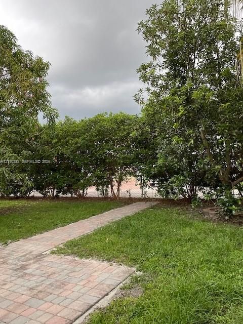 Backyard featuring a paved stone walkway, expansive lawn, mature trees, and chain-link perimeter fencing