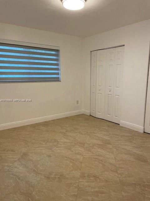 Room featuring large-format diagonal tile flooring, bi-fold closet doors, dual-layered adjustable window shades, and a flush-mount ceiling light fixture