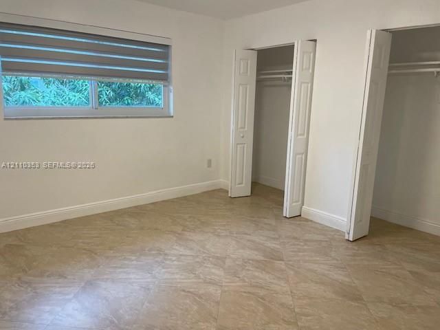 Room featuring neutral stone-finish tile flooring, dual closets with white bi-fold doors, and a horizontal window with retractable shades