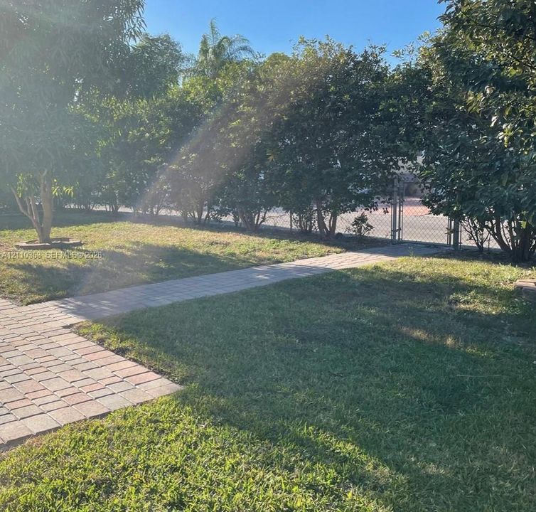 Backyard space featuring a paver walkway, lawn, mature trees, and chain-link fencing