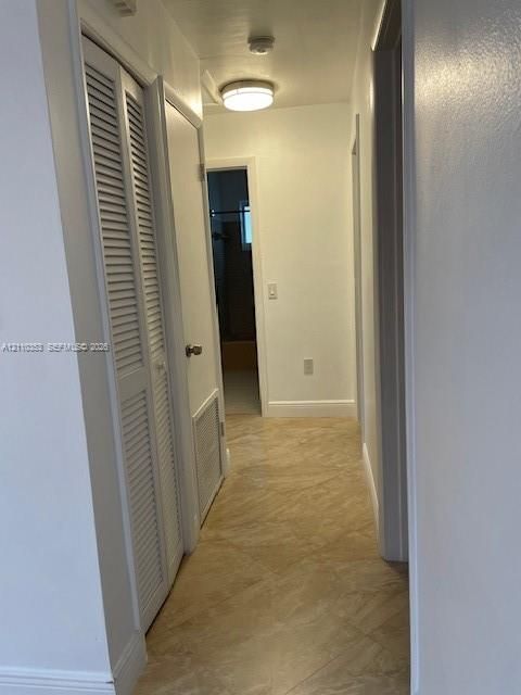 Hallway featuring tile flooring, louvered closet doors, and a flush-mount ceiling light fixture