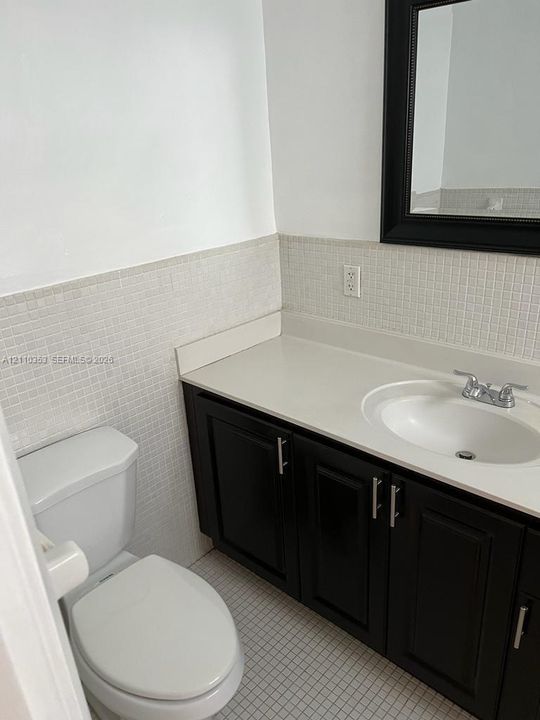 Dark-finish vanity cabinetry with brushed metal hardware, white solid-surface countertop, integrated basin, and neutral mosaic tile wall treatment