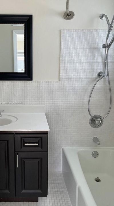 Dark cabinetry vanity with a solid surface countertop, white mosaic wall tile, and a shower-tub combination featuring a handheld shower head