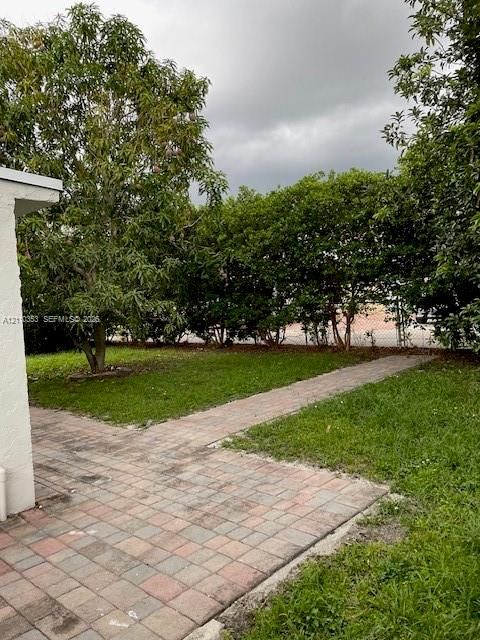 Backyard space featuring a paver patio, stone-tiled walkway, manicured grass, and mature foliage