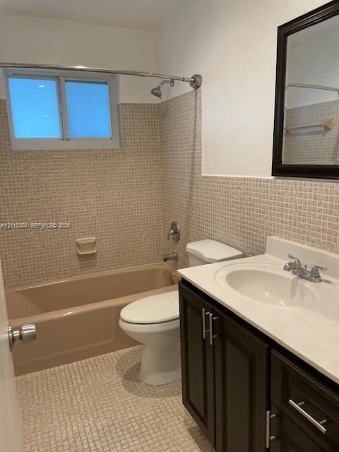 Bathroom featuring dark wood-finish cabinetry, white countertop with integrated sink, tiled wall surround, and a recessed bathtub