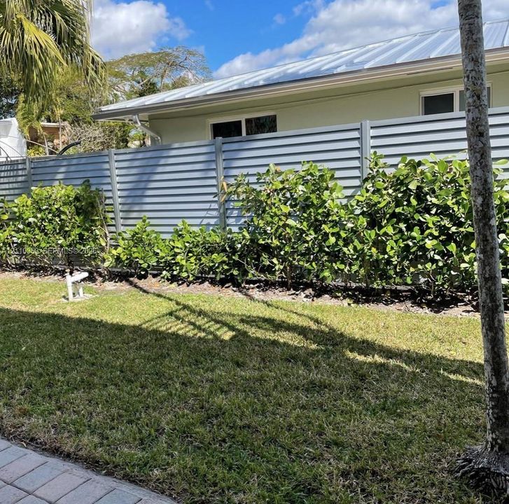 Metal-slat privacy fencing, manicured lawn, and mature ornamental shrubbery