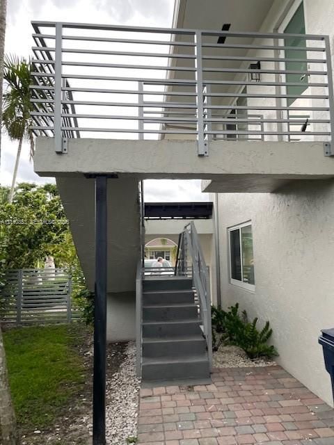 Exterior balcony featuring modern horizontal metal railings, concrete staircase, paver walkway, and stucco siding