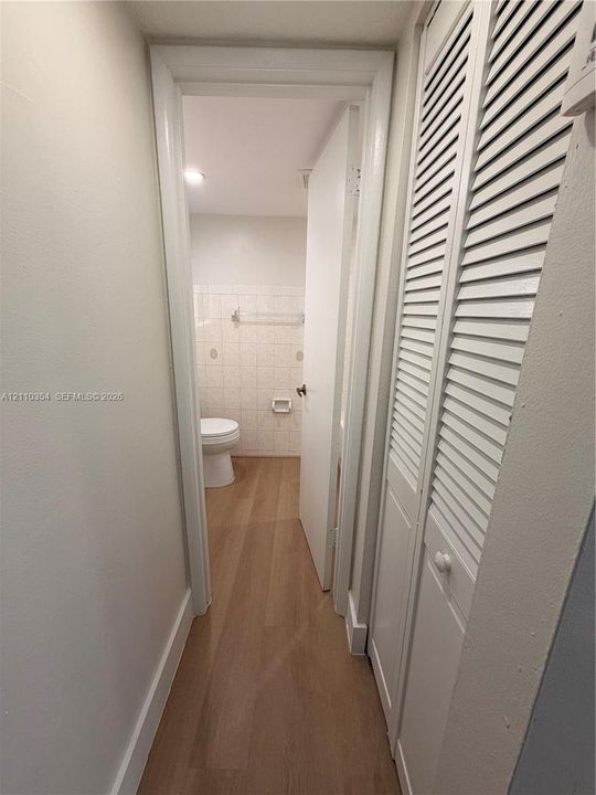 Hallway featuring wood-finish flooring and white louvered-door closets, leading to a space with tile-surround walls