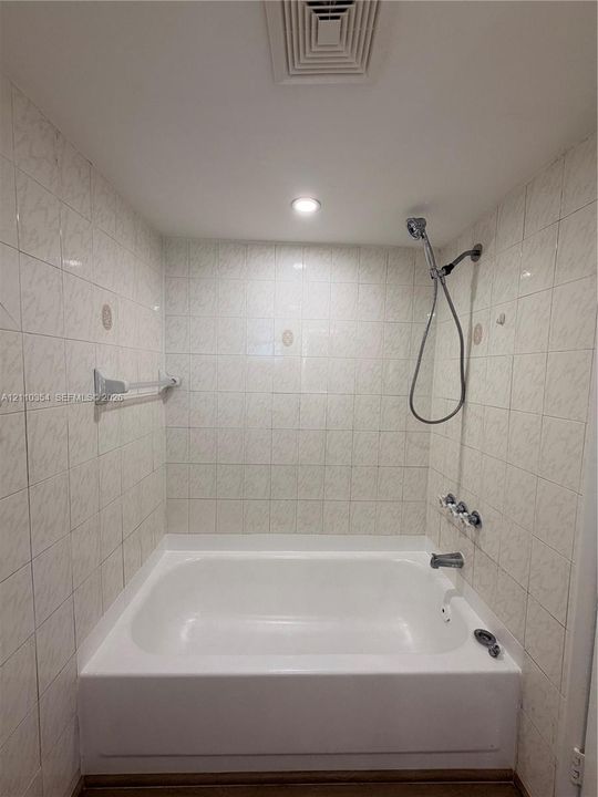 Alcove bathtub featuring white tile wall surround, chrome handheld shower fixture, integrated metal towel bar, and recessed lighting