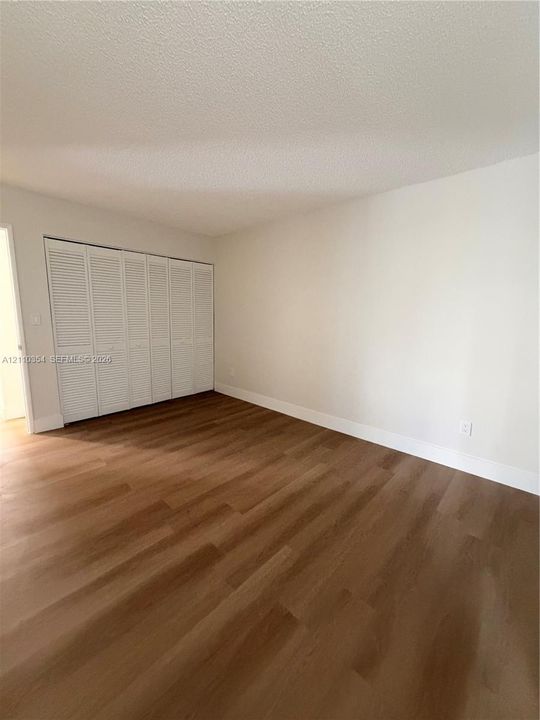 Room featuring wood-finish flooring, neutral walls, and a large reach-in closet with white louvered bi-fold doors