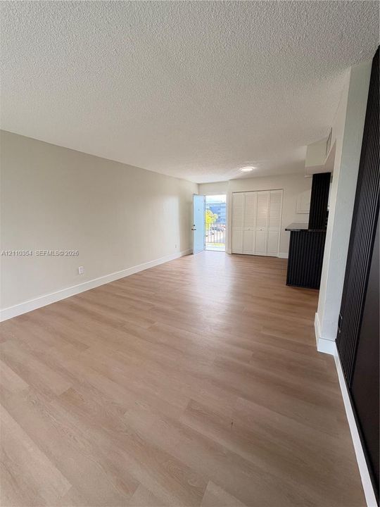 Open-concept living space featuring wood-finish flooring, neutral wall paint, floor-to-ceiling built-in closet cabinetry, and a dark-toned breakfast bar