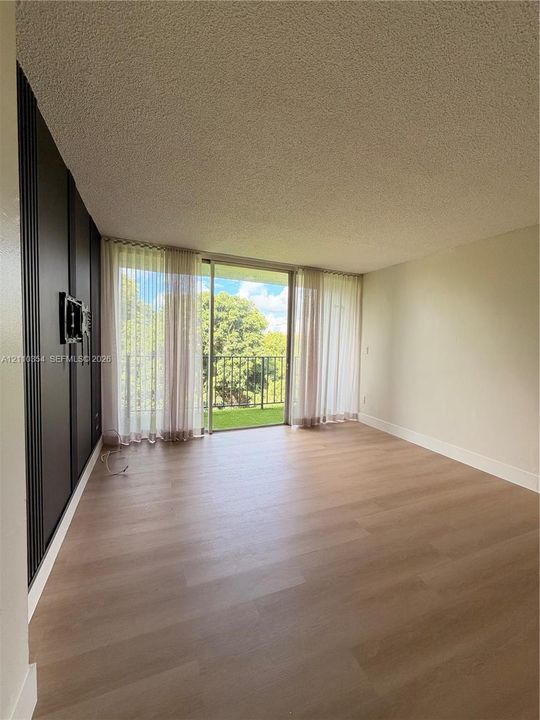 Wood-finish flooring, floor-to-ceiling sliding glass doors, decorative dark vertical paneling, and a metal-railed exterior balcony