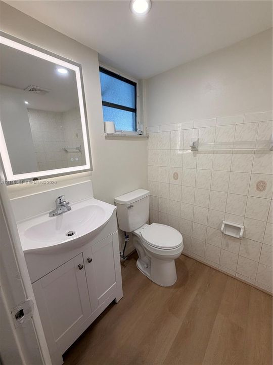 Bathroom featuring a vanity cabinet with a stone-top integrated sink, LED-backlit mirror, wood-finish flooring, and wall-mounted ceramic tiling