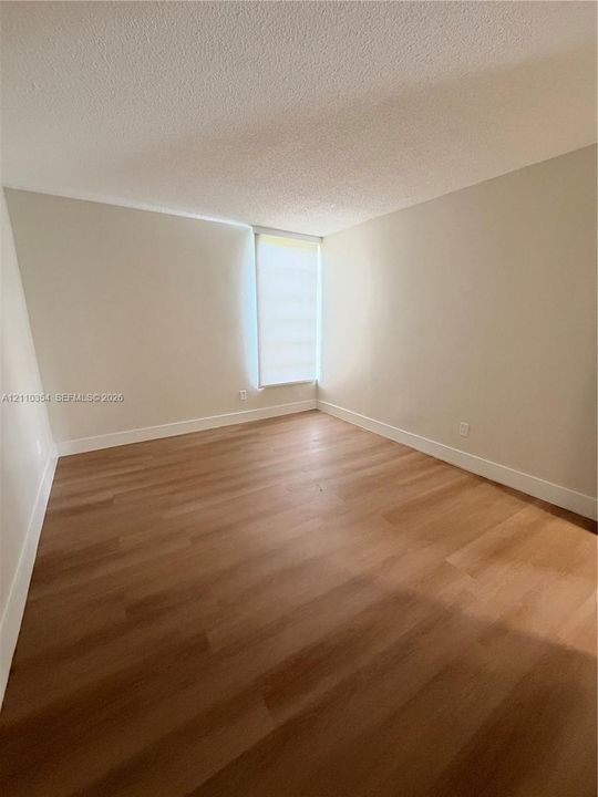 Neutral-toned walls, wood-finish flooring, and natural light entry through a vertical window with a roller shade