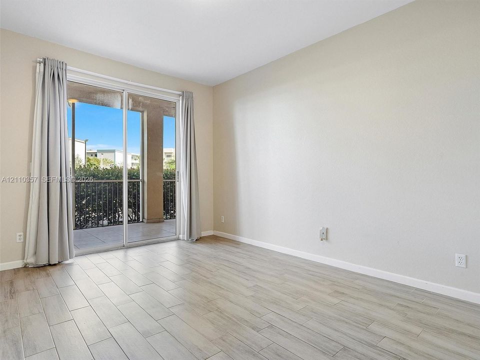 Neutral interior space featuring wood-finish flooring and floor-to-ceiling sliding glass doors opening to a private balcony with metal railing