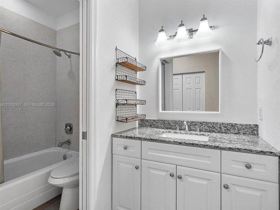 Bathroom featuring a white vanity with stone-patterned countertop, rectangular undermount sink, three-light fixture, and tub-shower combination with full-height tile surround
