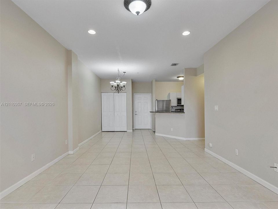 Open-concept interior featuring neutral wall tones, large-format tile flooring, recessed lighting, a decorative chandelier, and a breakfast bar with stone-finish countertops