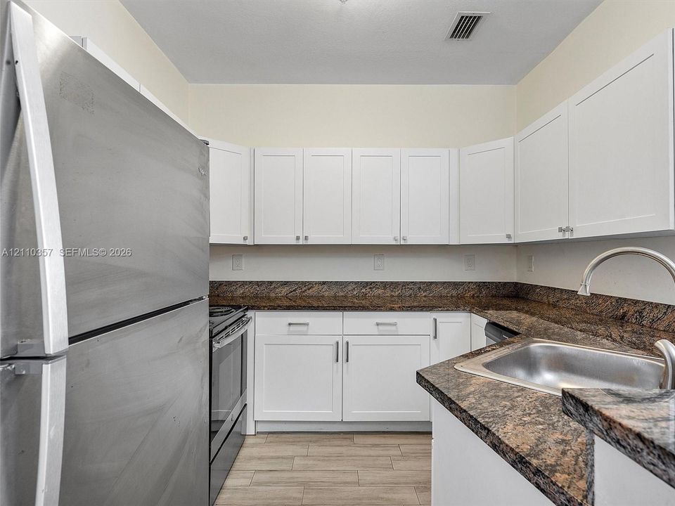Kitchen featuring white shaker-style cabinetry, stone-finish countertops, stainless steel refrigerator, stainless steel range, and wood-finish flooring