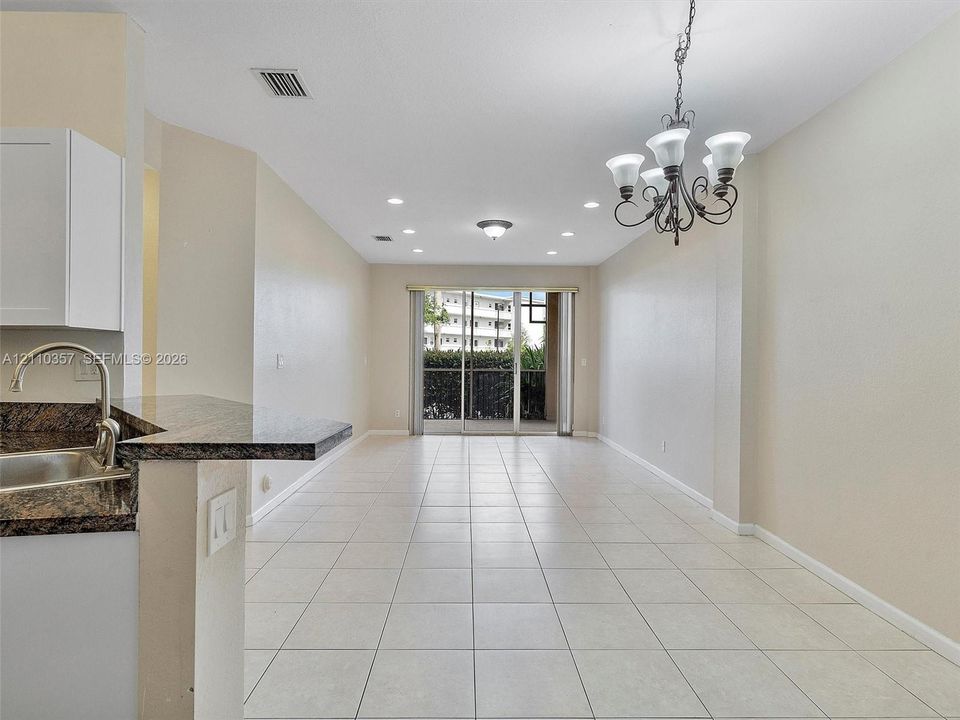 Open-concept area featuring stone-finish countertops, ceramic tile flooring, a multi-light chandelier, recessed lighting, and a glass sliding door